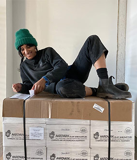 Lolly Lolly owner smiling and laying on top of a pallet of clay