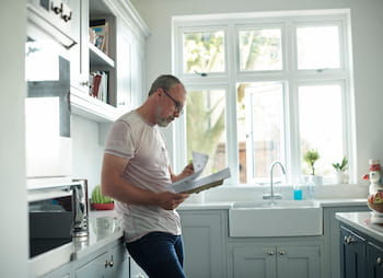 man reading mail leaning on kitchen counter