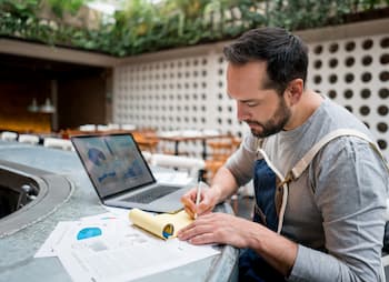 man sitting at bar with laptop and notepad