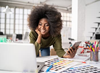 Woman designer checks Facebook on iPhone and laptop