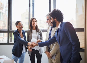 A group of business professionals are shaking hands with each other at an office 