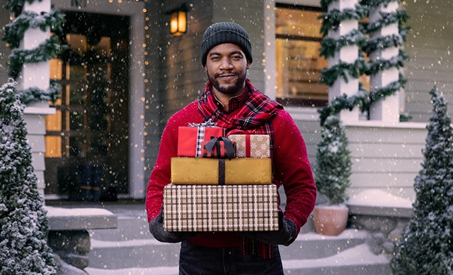 Hombre frente a una casa sosteniendo regalos