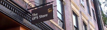 Cartel colgante fuera de un edificio de piedra rojiza con el logotipo de The UPS Store