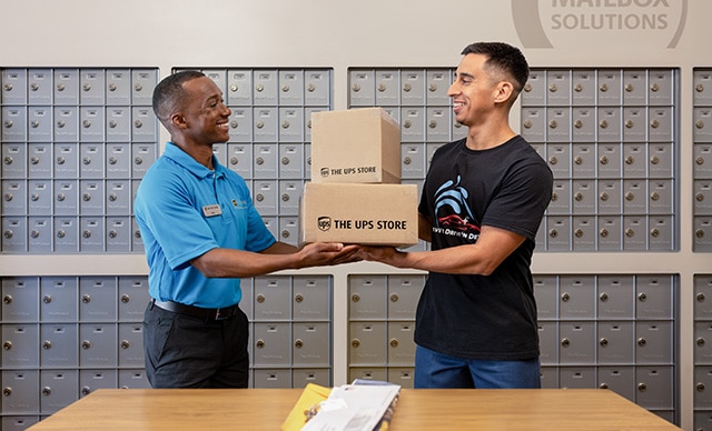 The UPS Store associate handing a customer packages in front of mailboxes