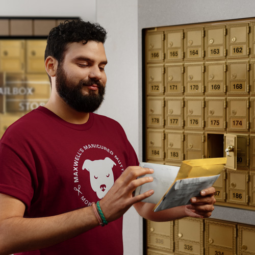 Man in a red shirt smiling, holding mail in hand in front of an open mailbox